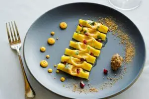 Casoncelli Pasta – Food Photography Plate of casoncelli pasta with sauce and garnishes, with folk on a white linen cloth bathed in soft light.