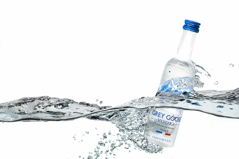 Grey Goose vodka bottle dynamically splashing through water against a clean white background, emphasizing freshness and luxury branding.