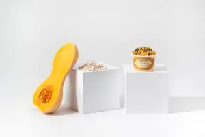 Three Sisters Beans – Product Photography A minimalist product setup featuring a meal cup alongside butternut squash, beans, and grains on white display blocks.