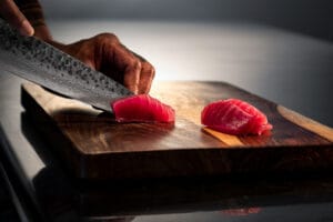 Chef slicing tuna for sushi on a wooden board using a Damascus chef"s knife.