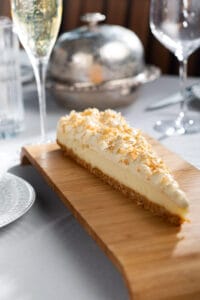 Slice of coconut cream pie topped with toasted coconut flakes, served on a wooden board.