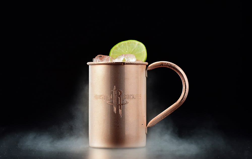 Moscow Mule in Copper Mug – Cocktail Photography A frosty Moscow Mule cocktail served in a branded copper mug, garnished with a lime wedge against a smoky black backdrop.