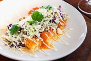 Entomatadas topped with shredded cabbage, fresh cilantro, and drizzled with creamy white sauce on a white plate.