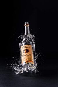 Exploding Tito’s Bottle Drink Photography A dynamic shot of a Tito's Handmade Vodka bottle shattering mid-air, creating an explosion of glass pieces.