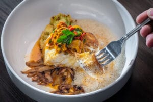 Halibut with pickled mussels, sambuca, and fennel pollen broth, with a fork lifting a piece.