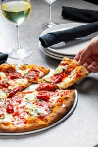 Pizza Slice – Food Photography Hand reaches taking a slice of pizza with wine.