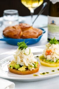 Fresh heirloom tomato slices topped with king crab and avocado, served on a white plate.