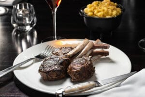 Grilled Lamb Chops with Mashed Potatoes – Food Photography Grilled lamb chops served with a side of mac and cheese and a glass of red wine in an elegant setting.