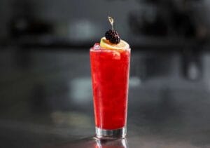 Vibrant lemon blackberry cocktail in a highball glass, garnished with a lemon wheel and fresh blackberries, set against a dark, moody background.