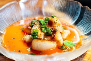 Lychee scallops garnished with green herbs and served in a unique glass bowl.