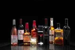 Assortment of wine and whiskey bottles with filled glasses in a row.