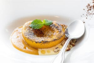 Roasted peach with Epoisse cheese, garnished with mint leaves, served in a white dish with a spoon.