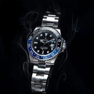 Rolex GMT Master Watch – Product Photography A Rolex GMT Master II watch with a blue and black bezel, dramatically lit with a smoky atmosphere on a black background.