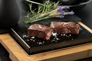 Close-up of Grilled Wagyu Sukiyaki steak on a black stone plate garnished with fresh rosemary.